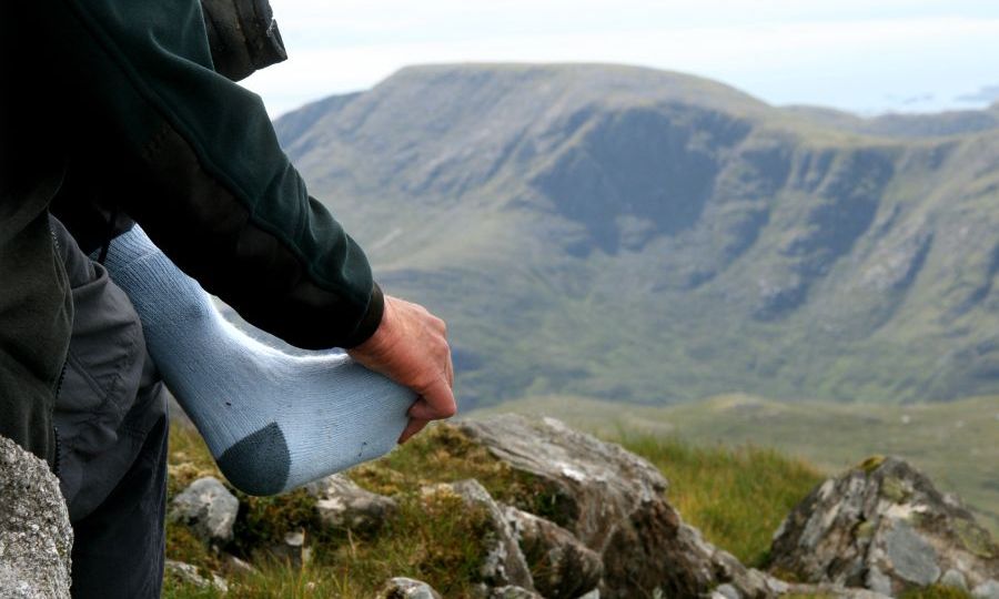 persona tocando su pie sobre el calcetín al lado de un paisaje montañoso